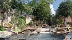 An outdoor patio area with wooden picnic tables and wicker chairs, surrounded by greenery and a stone wall. - The Fat Badger (York)