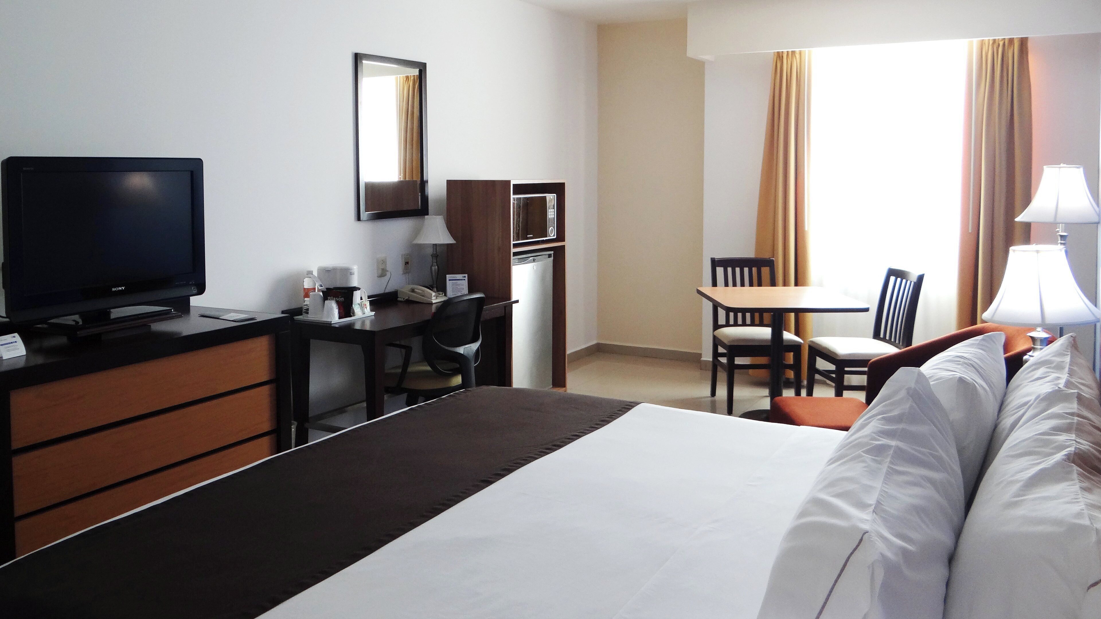Une chambre d’hôtel comprenant un lit, un bureau avec un ordinateur, une télévision, une chaise et une table à manger.