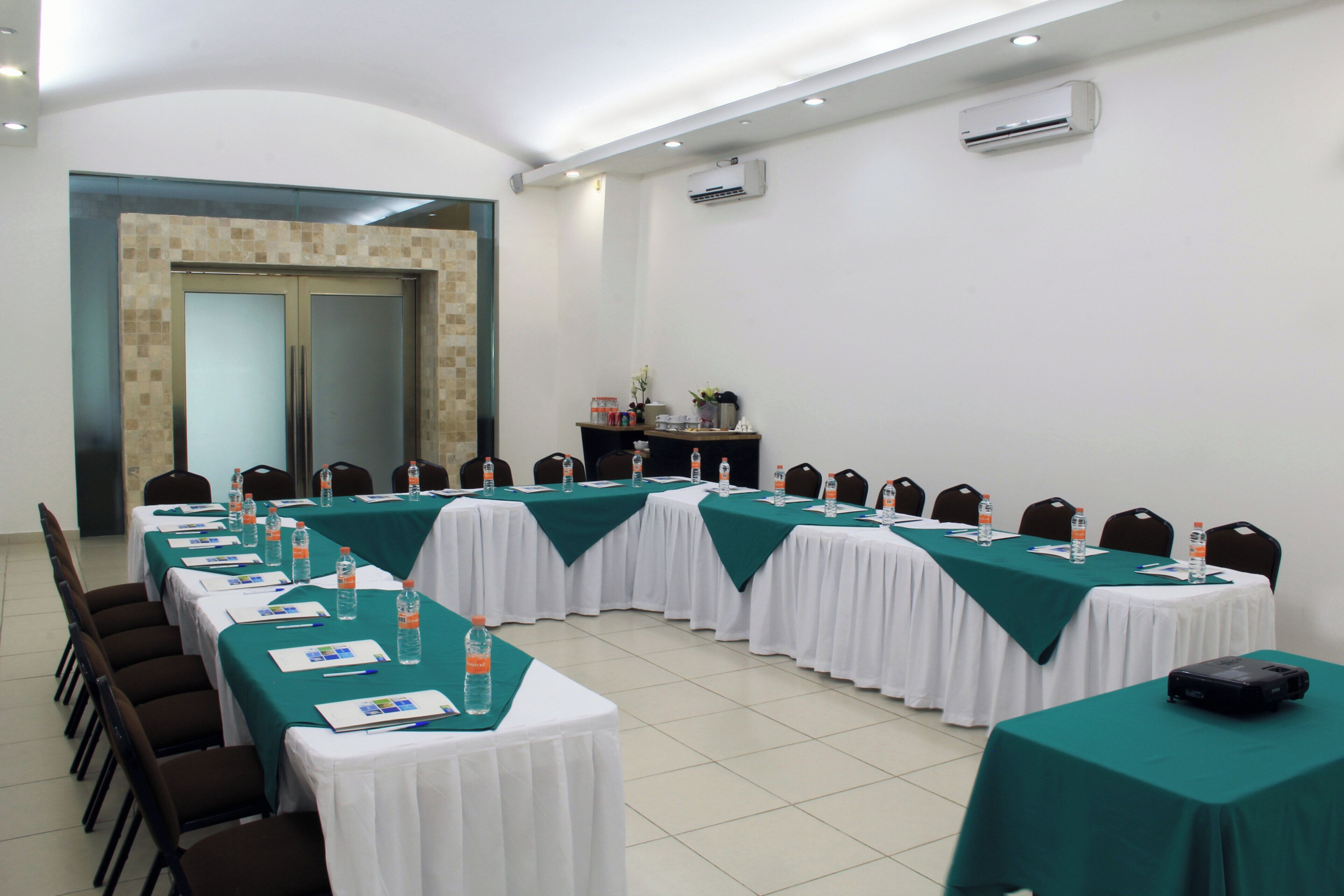 Un salón de conferencias con mesas dispuestas para una reunión, equipado con botellas de agua y tarjetas de identificación.