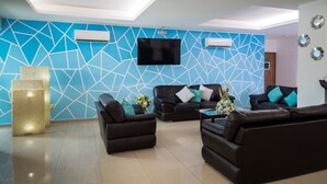 A modern living room with geometric wall design, a flat-screen TV, and leather sofas.