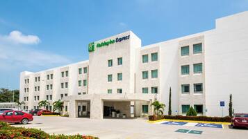 Un hotel Holiday Inn Express con fachada moderna, varios ventanales y un estacionamiento con espacios reservados para discapacitados.