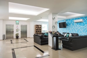 Un espace d’accueil moderne comprenant un comptoir de réception, un coin salon et un mur orné d’un motif bleu.