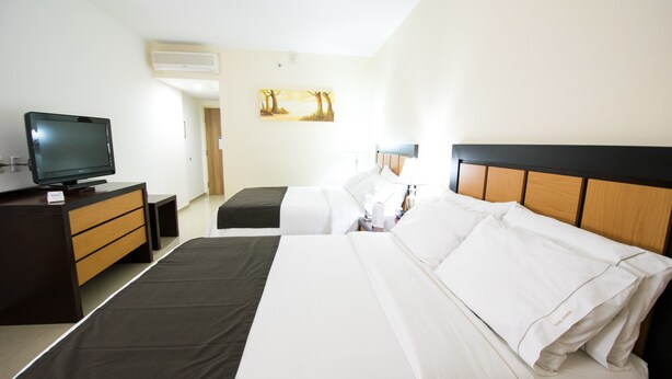 A hotel room with two beds, a TV, a desk, and a painting on the wall.