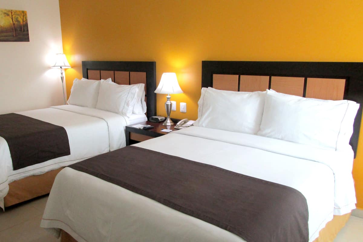 Une chambre d’hôtel avec deux lits, chacun étant équipé de draps blancs et d’une couverture marron. Il y a deux tables de chevet avec des lampes et un téléphone.