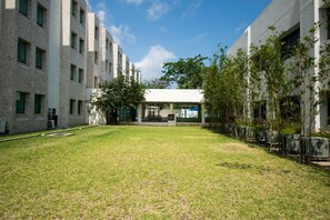 Une cour intérieure avec un bâtiment doté d’un espace de repos abrité, entourée d’arbres et d’une pelouse.