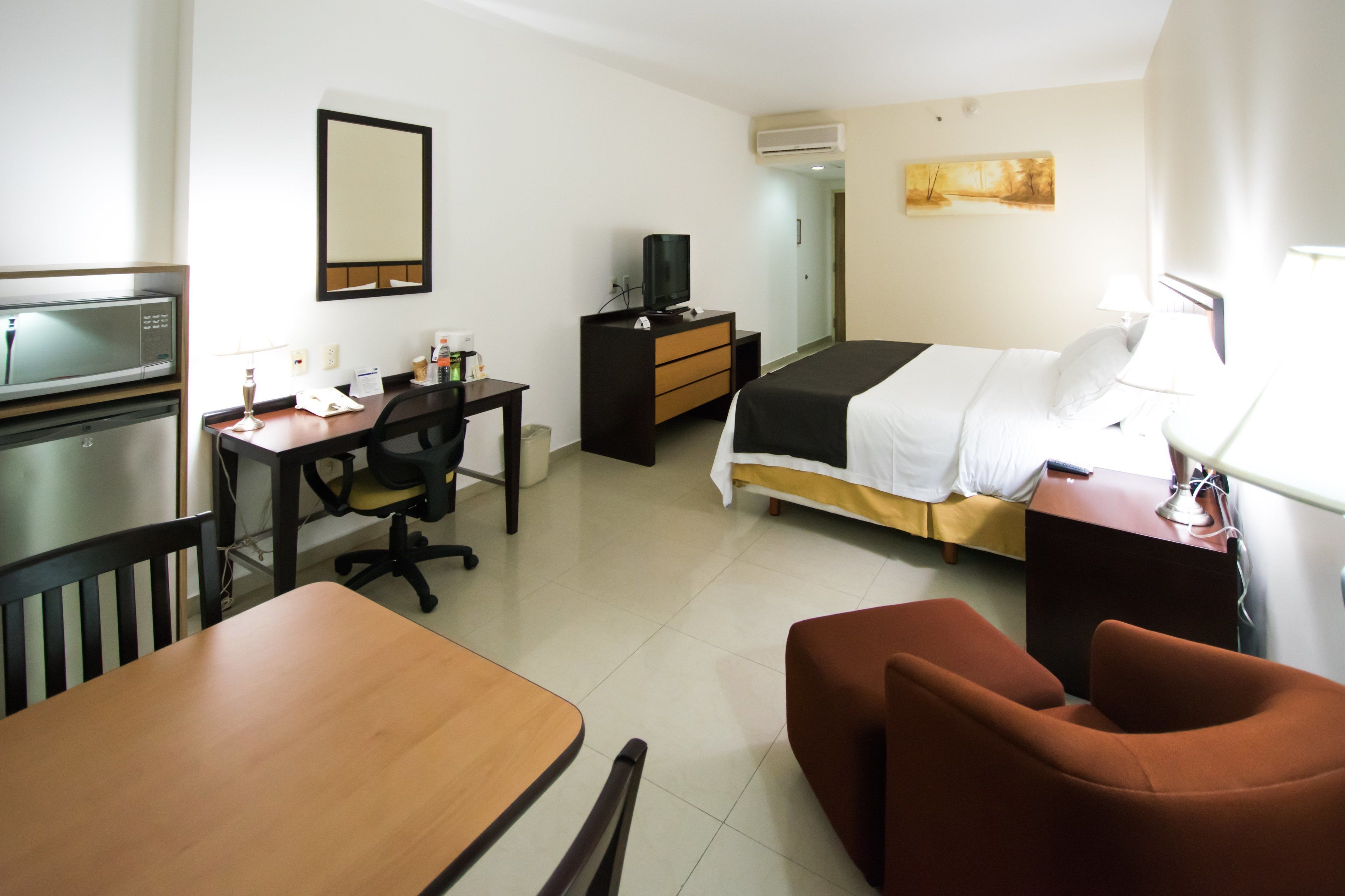 Habitación de hotel con cama, escritorio, silla, televisión y una pequeña mesa.