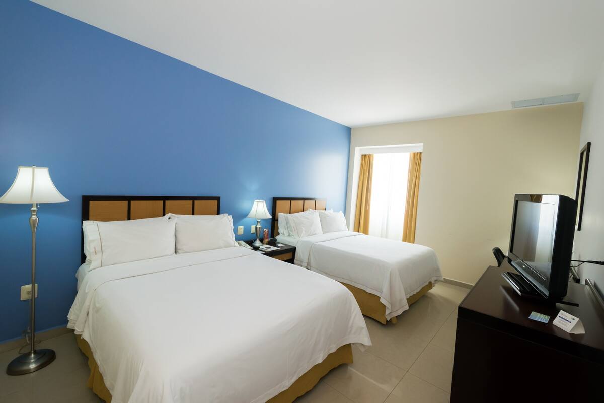 Une chambre d’hôtel avec deux lits, un bureau avec une télévision et une lampe.
