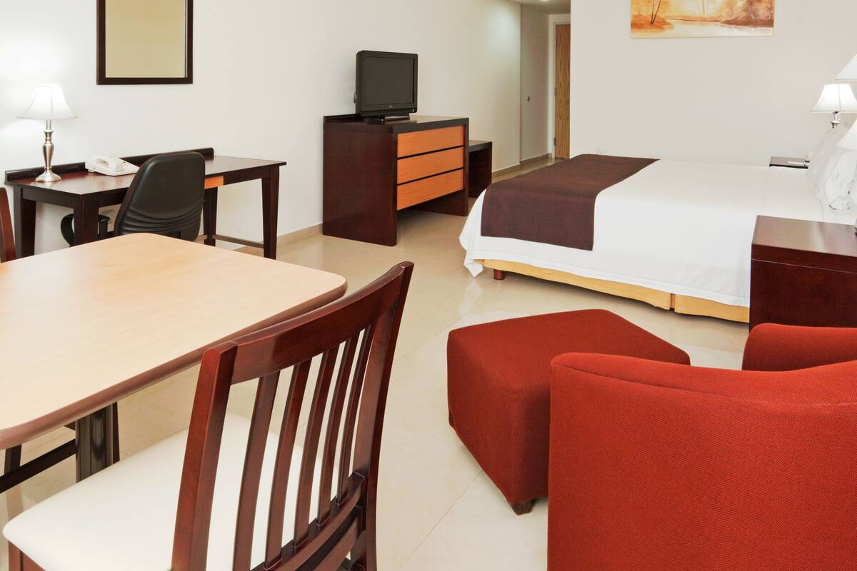 Une chambre d’hôtel avec un lit, un bureau et une chaise, une télévision, une commode et un canapé rouge.