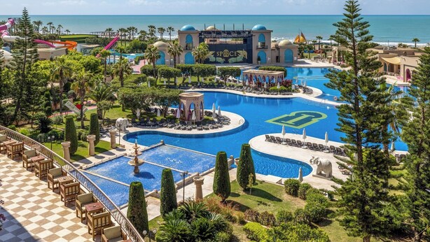 A resort with multiple swimming pools, palm trees, and a view of the ocean.