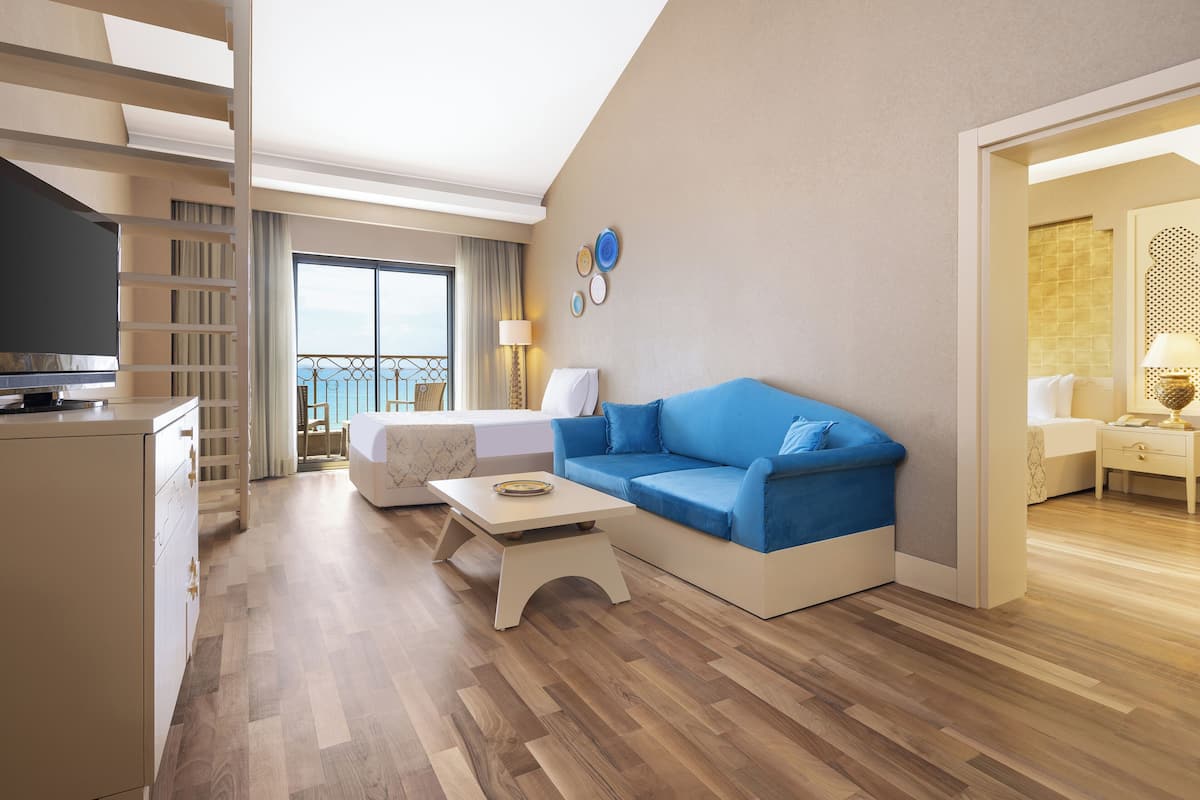 Ein modernes Hotelzimmer mit einem blauen Sofa, einem kleinen weißen Couchtisch, einem Fernseher und einem Balkon mit Blick.