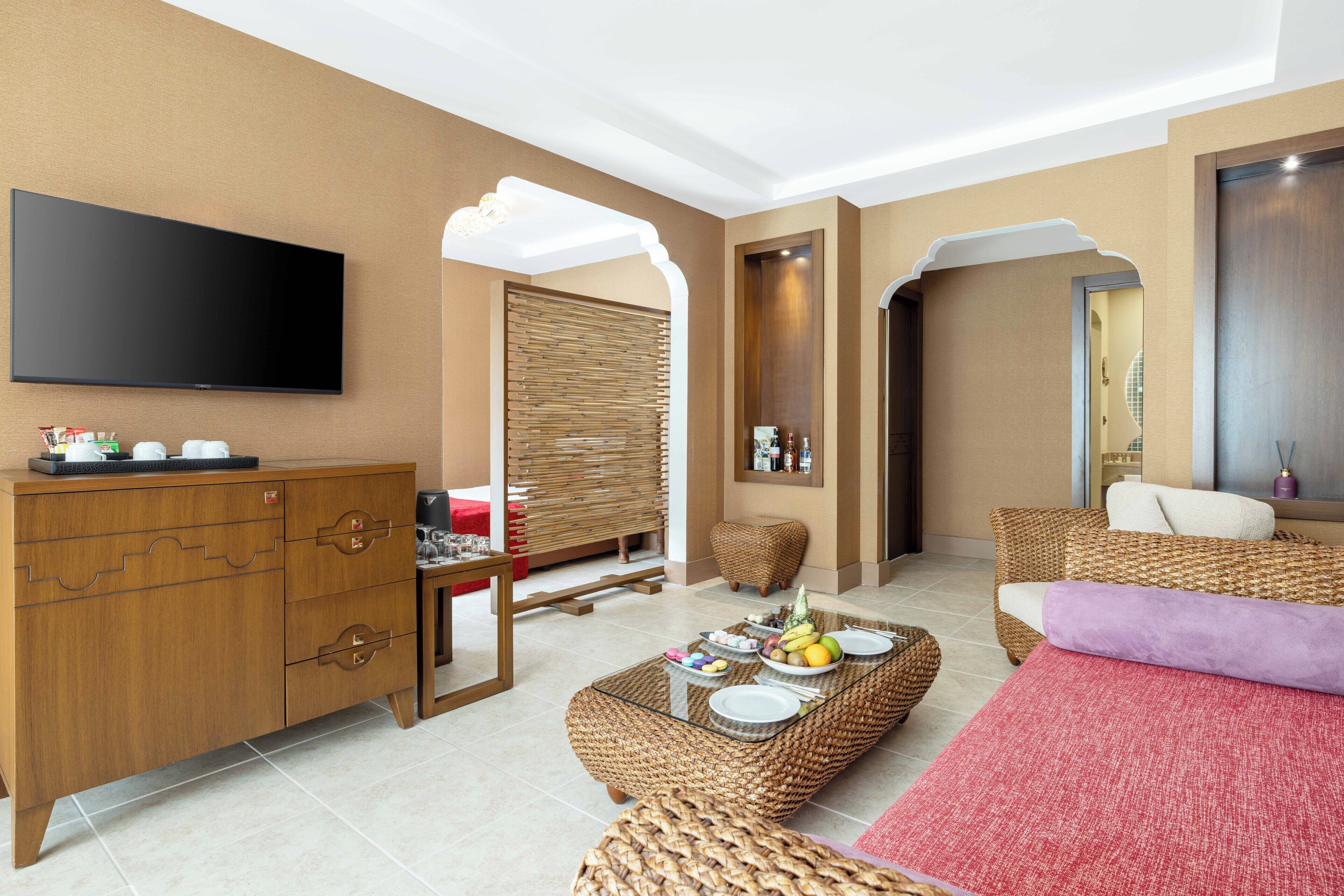 Een moderne hotelkamer met een flatscreen televisie, een houten kast, rieten meubels en een rode vloerkleed.