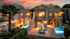 A hotel with a pool area, lounge chairs, and a sunset sky.