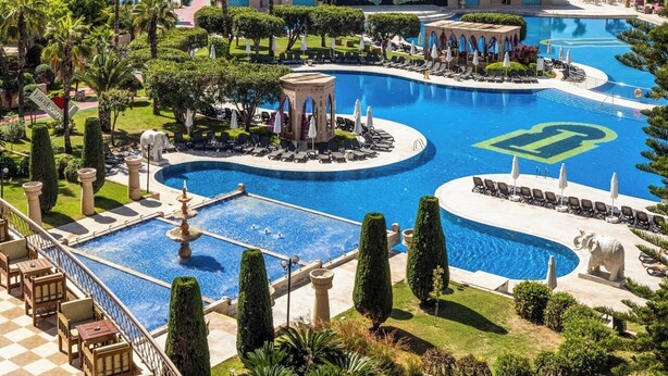 A resort with a large central pool, multiple smaller pools, and a view of the ocean.
