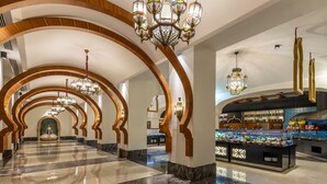 A hotel lobby with a marble floor, arched wooden columns, chandeliers, and a food bar.