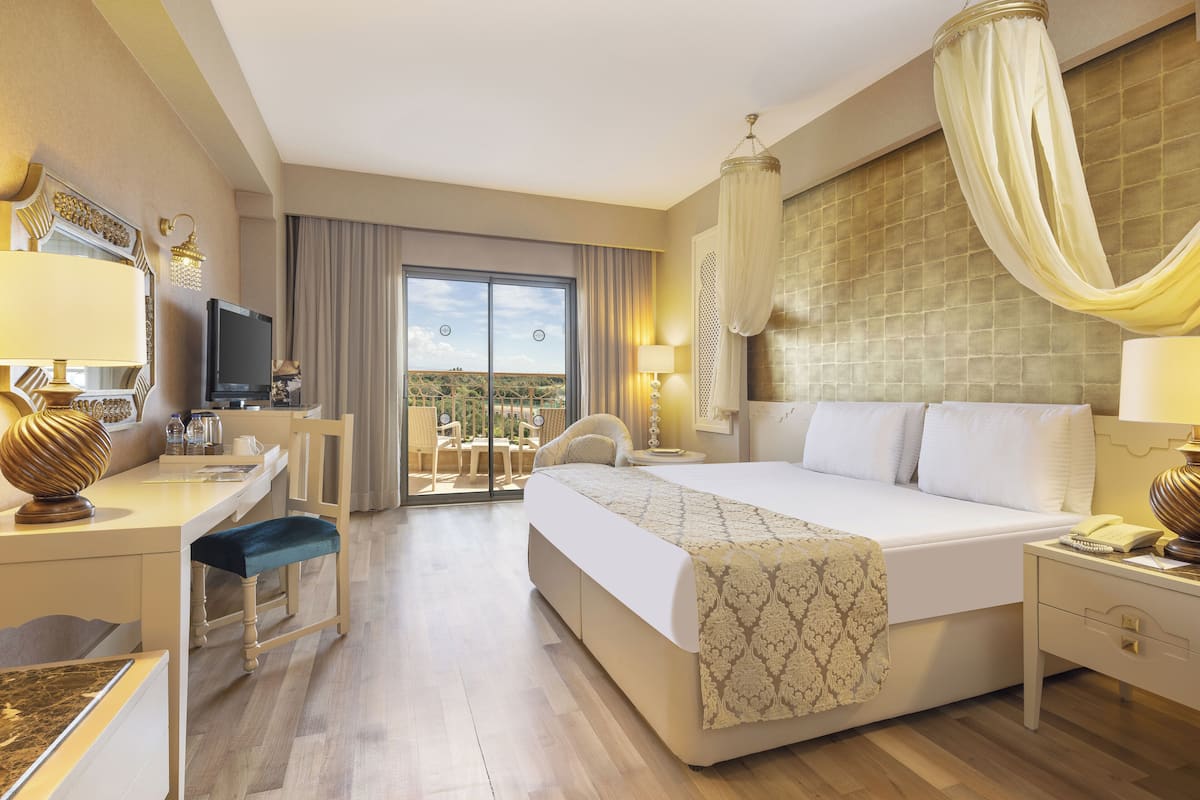 Ein Hotelzimmer mit einem großen Bett, einem Schreibtisch mit Stuhl, einem Fernseher und einem Balkon mit Blick.