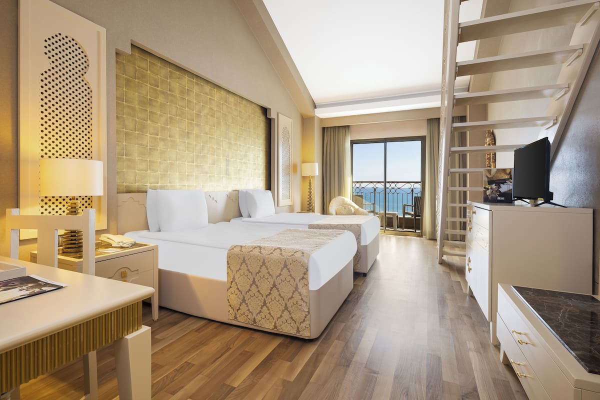Ein Hotelzimmer mit einem großen Bett, einem Schreibtisch, einem Sessel, einem Fernseher und einem Balkon mit Blick.