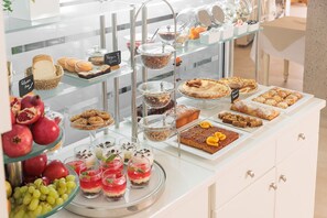 A buffet with various food items including pastries, desserts, and fruits. - Iria Beach art hotel (Naxos)