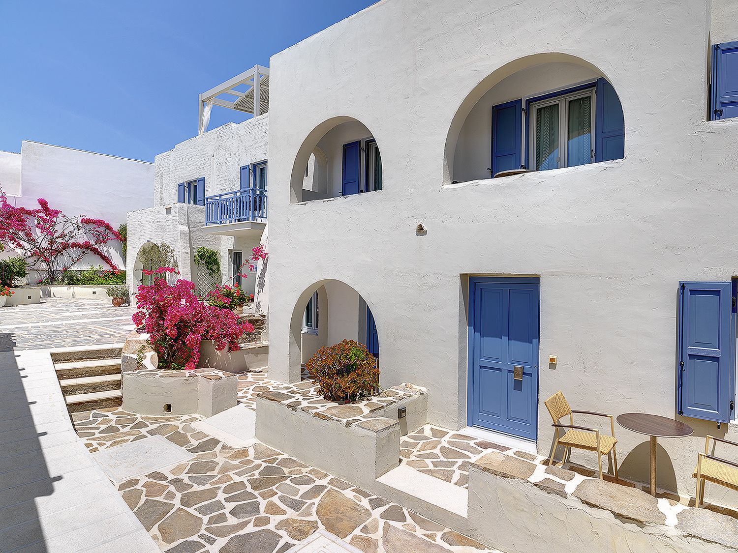 A white building with blue doors and windows, stone steps, and a small table with chairs.