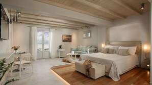 A modern bedroom with a large bed, a seating area, and a view of the outdoors. - Iria Beach art hotel (Naxos)