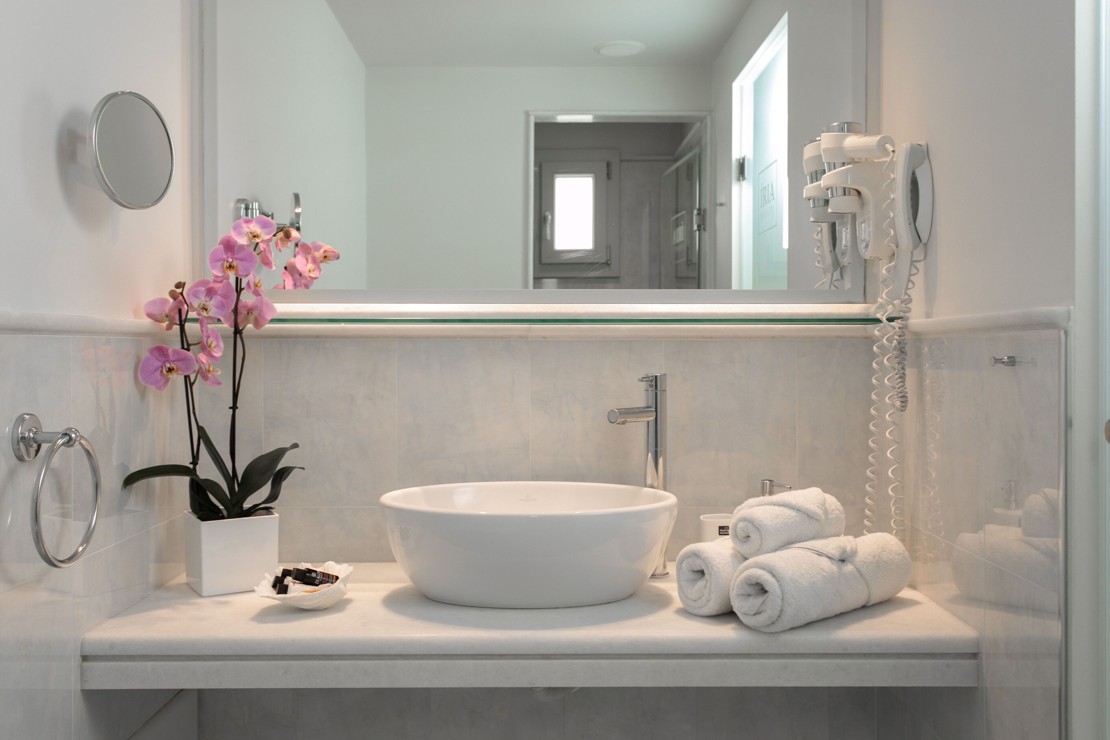 A bathroom with a white sink, a mirror, a towel rack, a potted orchid, and a hairdryer.
