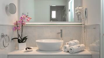 A bathroom with a white sink, a mirror, a towel rack, a potted orchid, and a hairdryer.