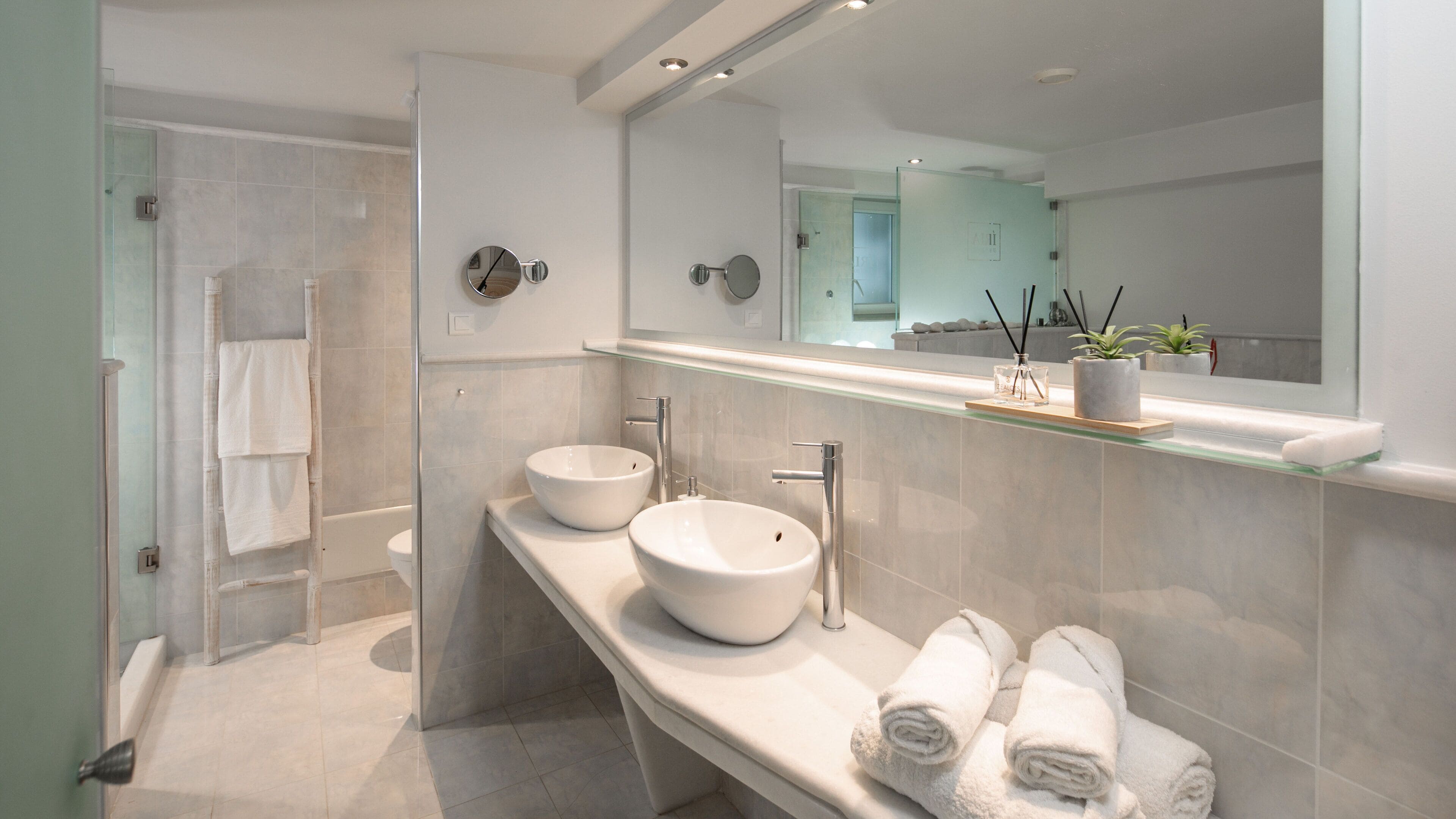 A modern bathroom with two sinks, a glass shower enclosure, and a mirror with a shelf above.