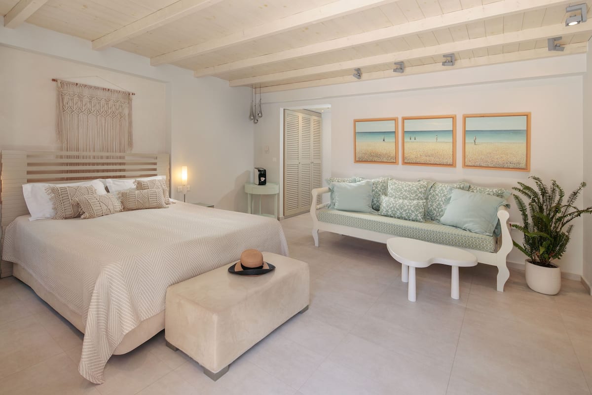Een slaapkamer met een bed, een bankje, een slaapbank en een potplant.