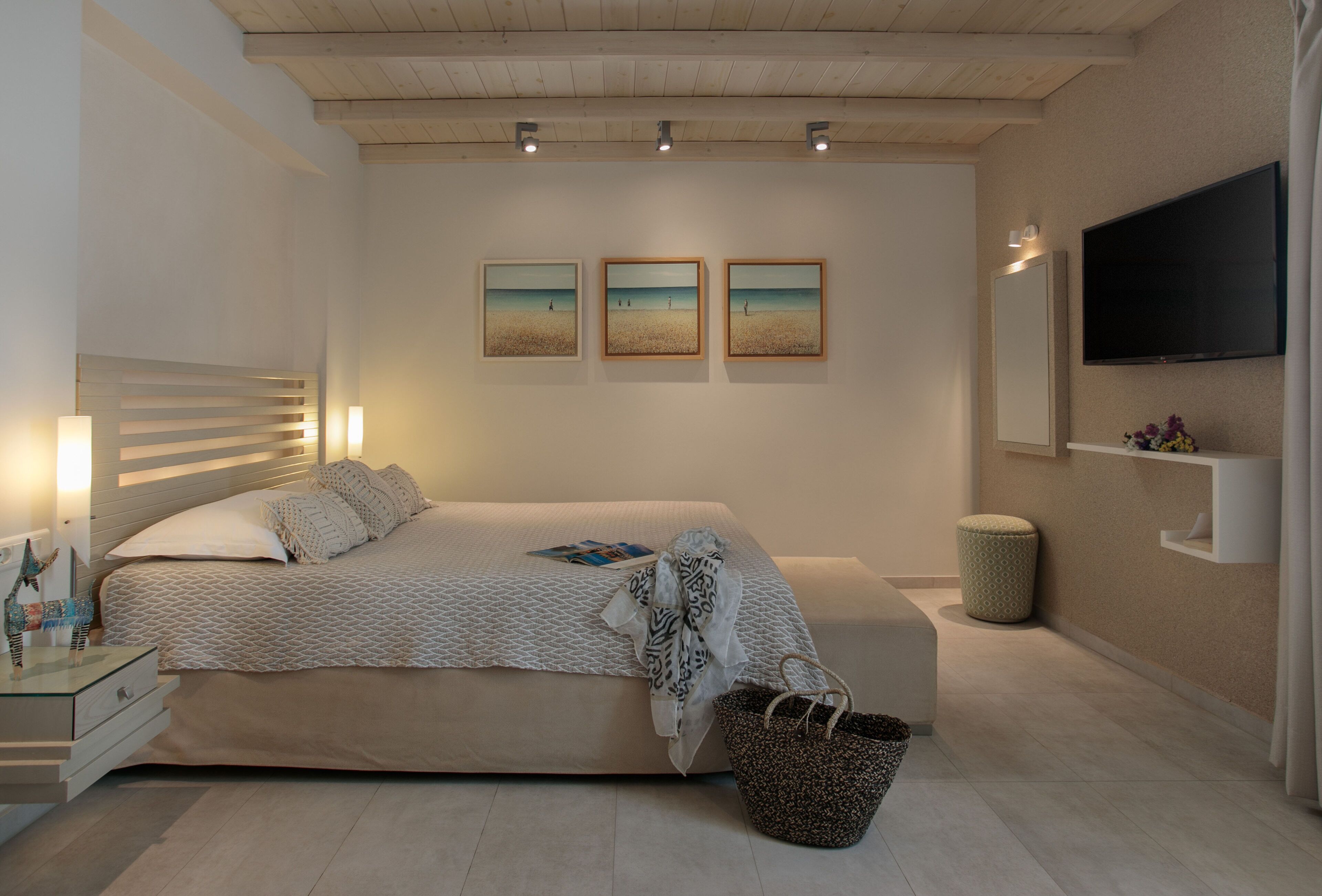 A modern bedroom with a large bed, bedside tables, a TV, and artwork on the wall.