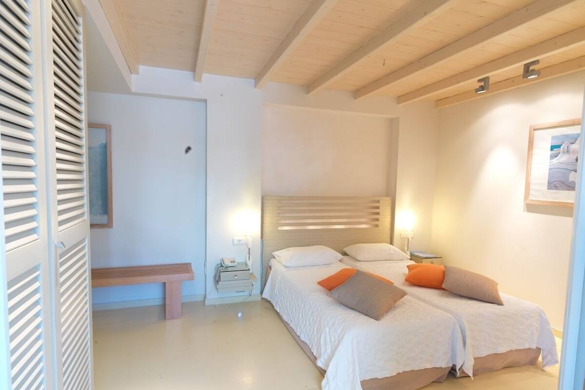Slaapkamer met twee bedden, een bankje, nachtkastjes en een wandlamp.