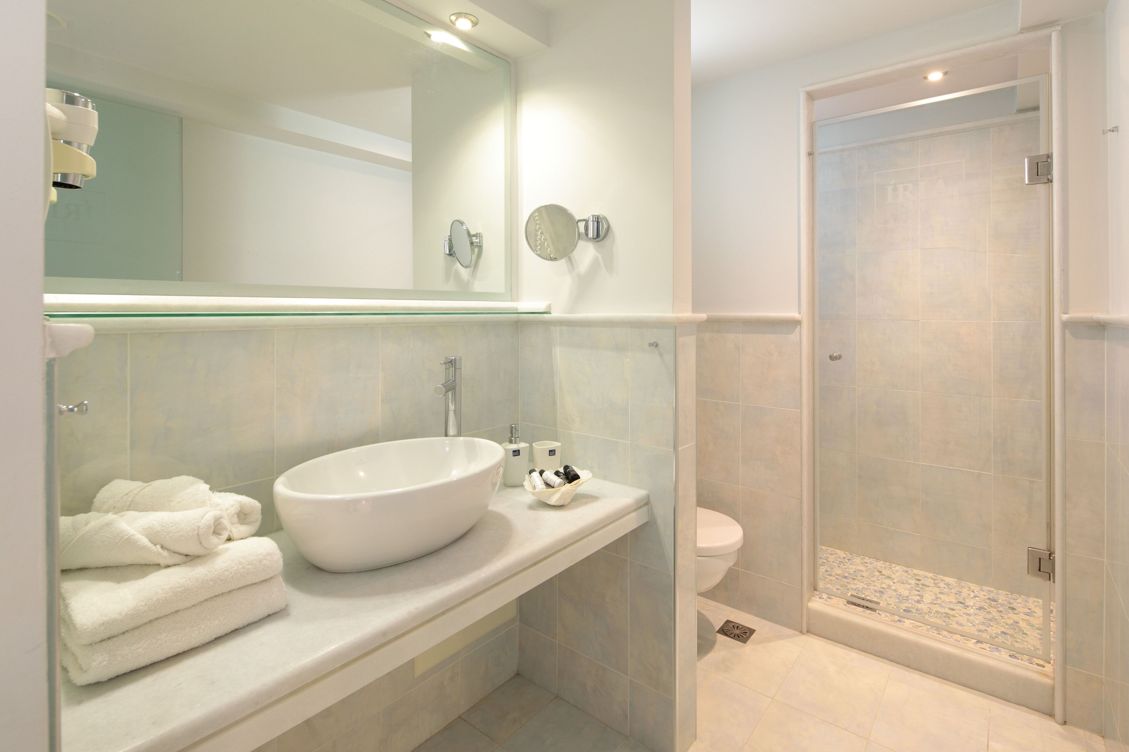 Un bagno moderno con un lavandino bianco capiente, un box doccia in vetro e un water.