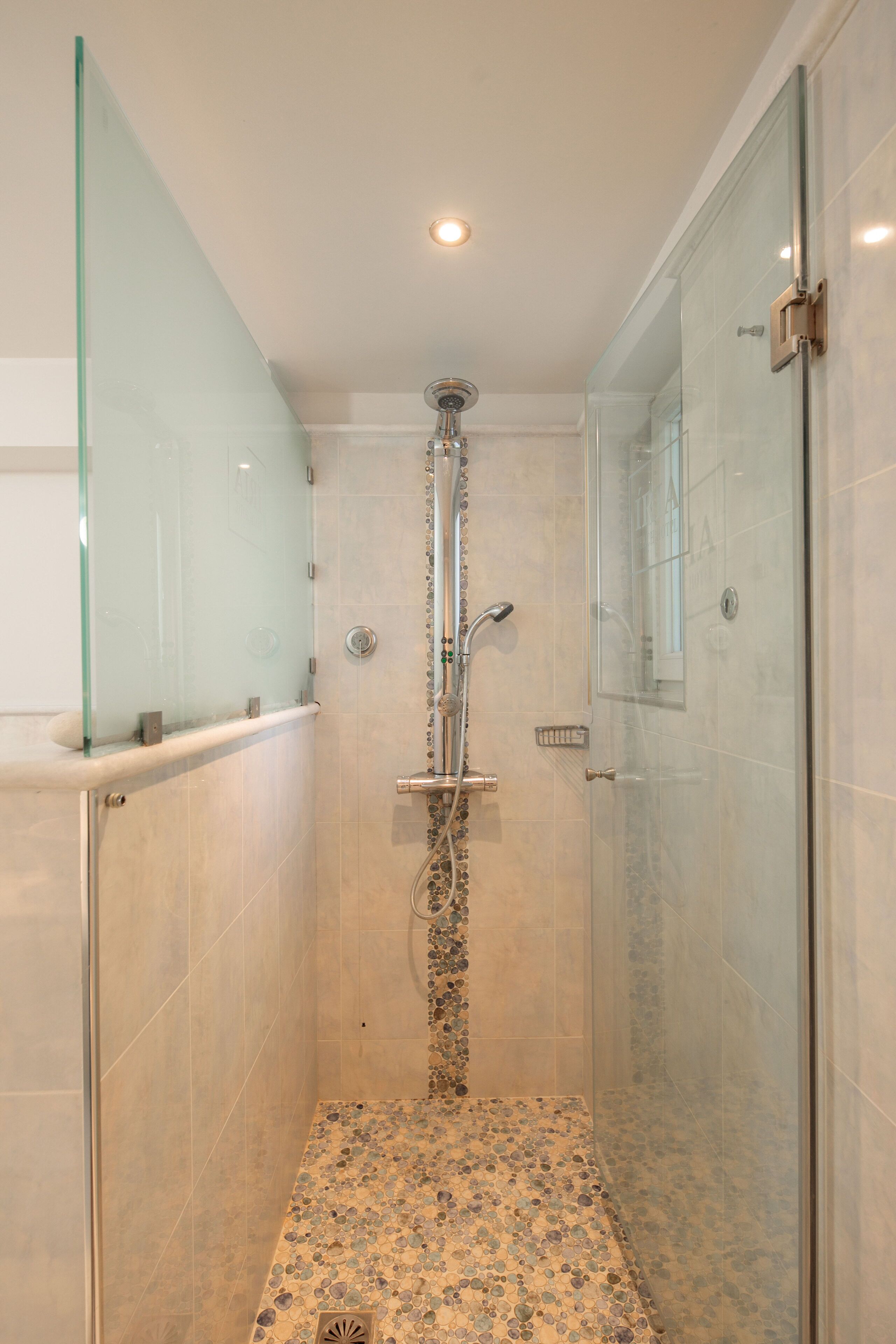 A glass-enclosed shower with a tiled floor and a glass partition on one side.