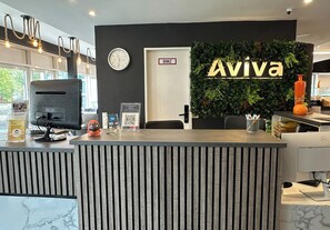 A reception desk with a digital clock, a sign reading 'Aviva,' and a QR code. - Hotel AVIVA by APOLONIA (Karlsruhe)