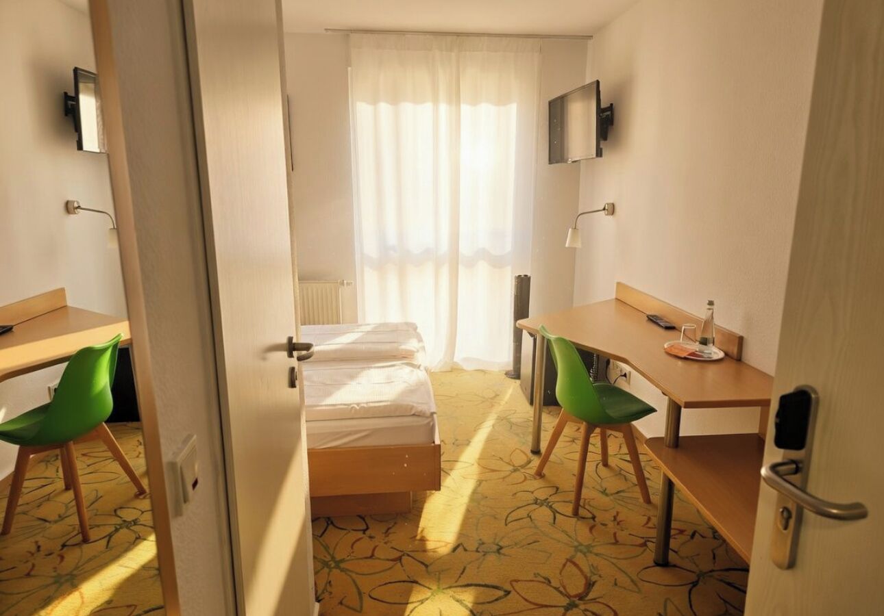 A hotel room with a bed, a desk, two chairs, a television, and a window with curtains.