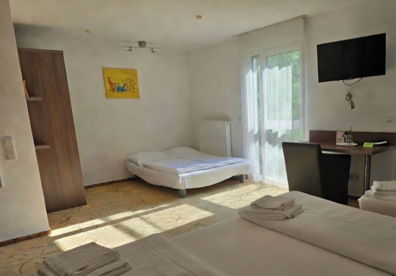 A hotel room with a bed, a desk, a chair, a TV, and a window.