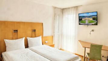 A hotel room with a double bed, a desk, a chair, a television, and a window with curtains.