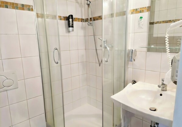 Zona de ducha con mampara de vidrio, cabezal de ducha de mano y grifo empotrado.