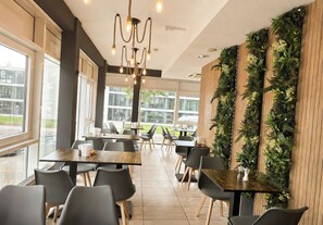 Un comedor moderno con mesas y sillas, ventanas amplias y una pared decorativa con plantas.