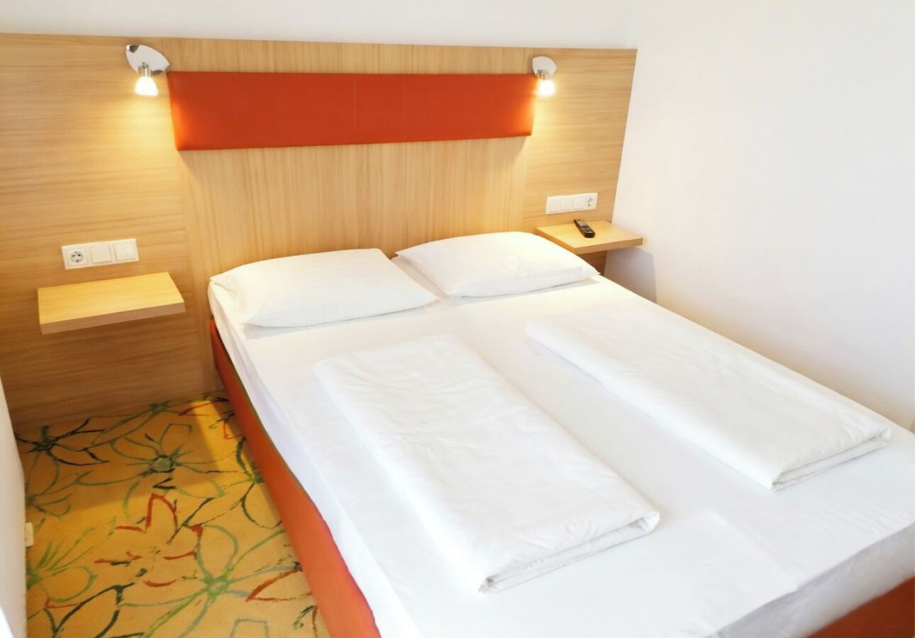 A single bed with white linens, a wooden headboard, and bedside tables with lamps.