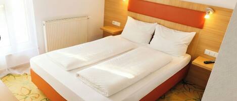 Cama doble con cabecera de madera y dos mesitas de noche, una con lámpara.