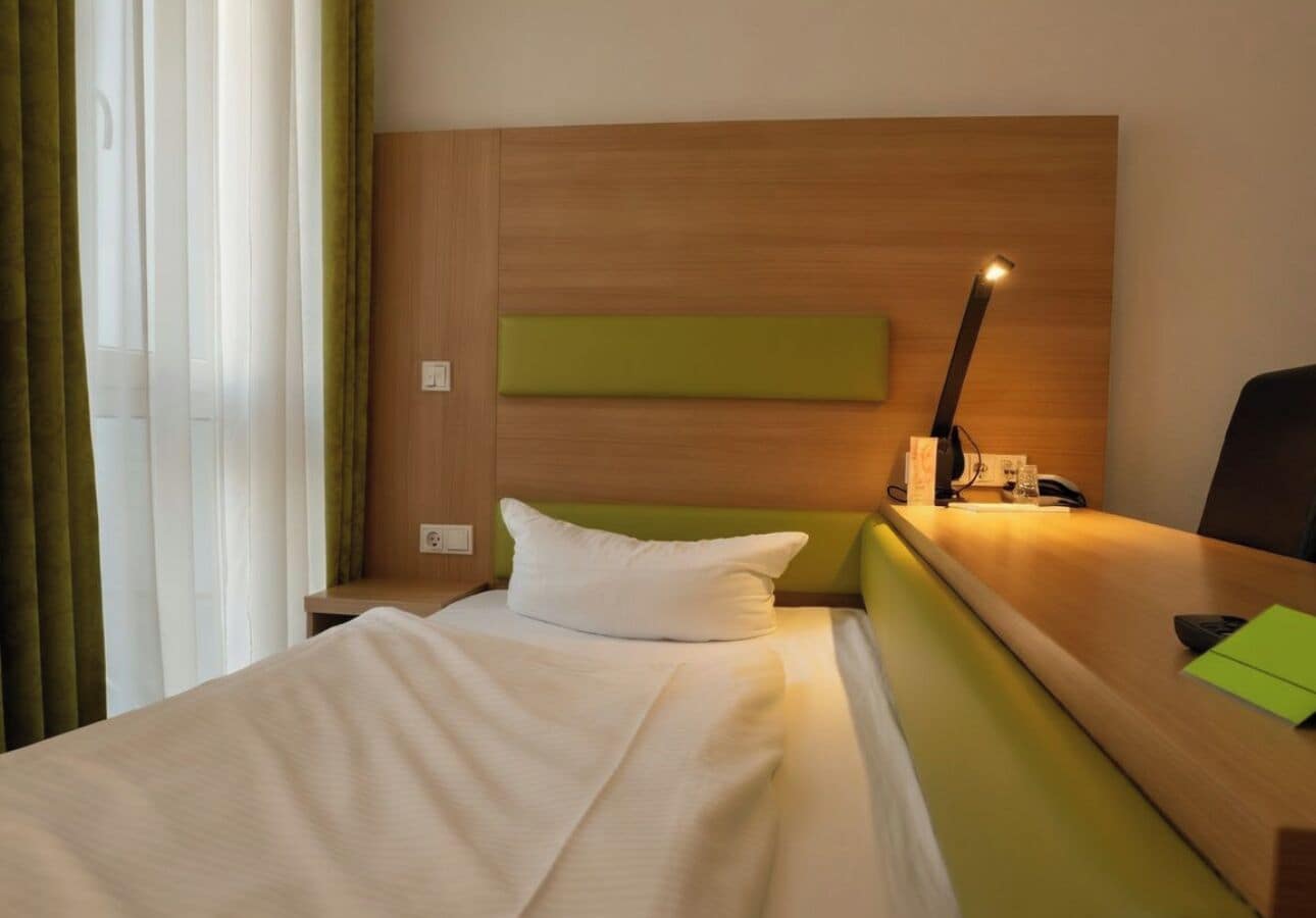 Ein Hotelzimmer mit einem Bett, einem Nachttisch, einer Lampe und einer Wand in Grüntönen.