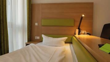 Ein Hotelzimmer mit einem Bett, einem Nachttisch, einer Lampe und einer Wand in Grüntönen.