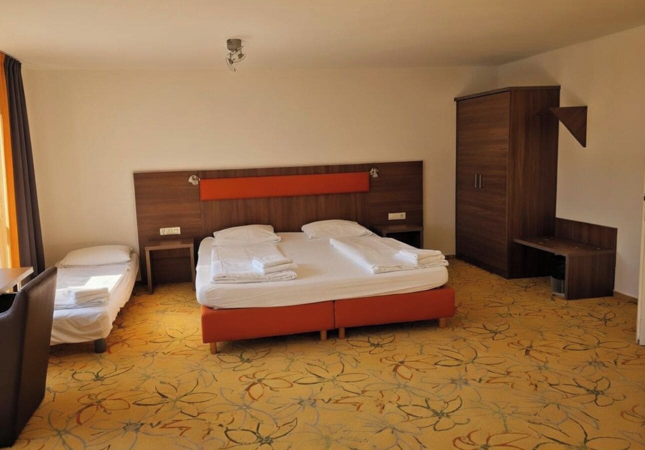 A hotel room with a bed, a nightstand, a wardrobe, and a small table.