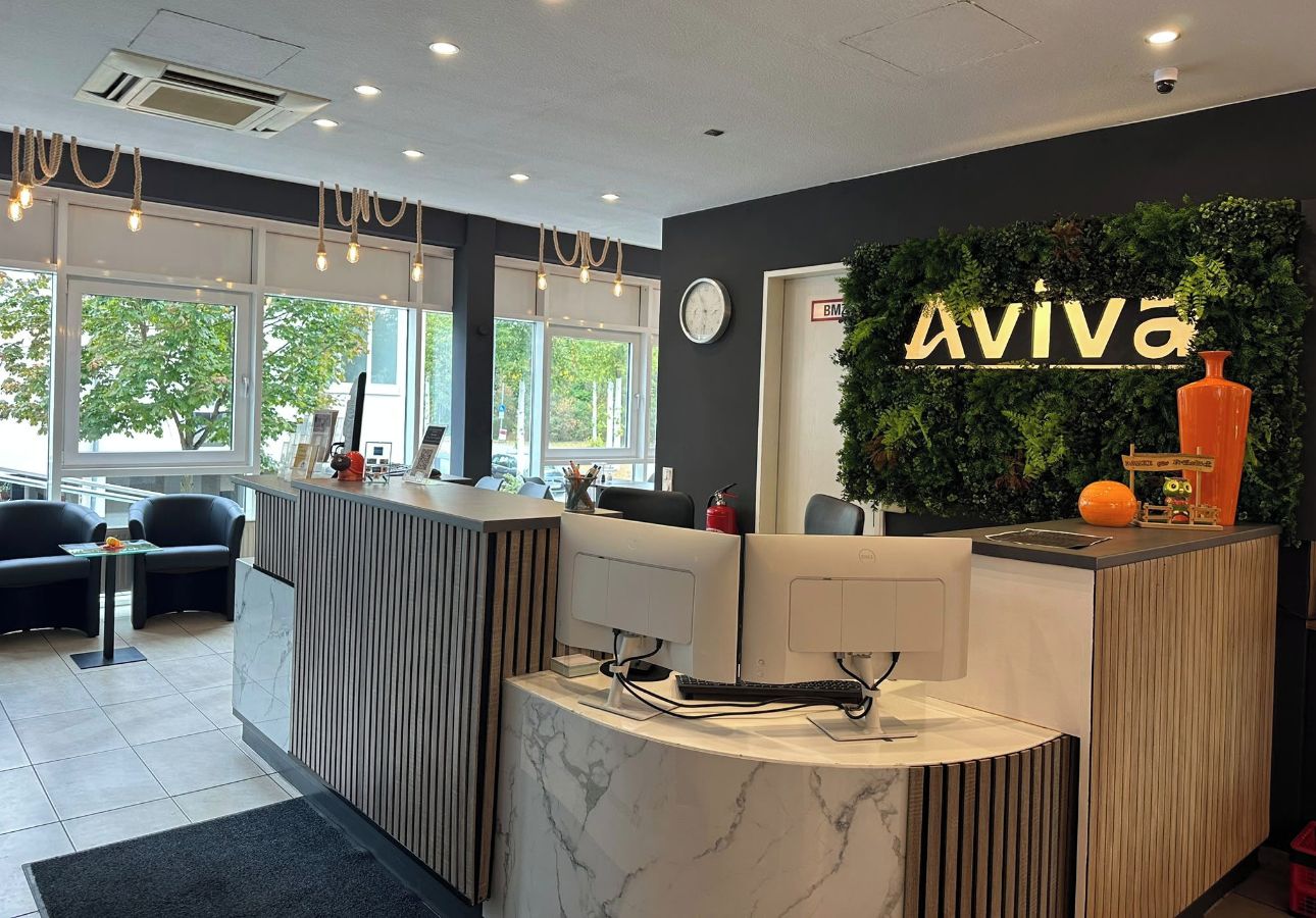 A reception area with a marble counter, a clock, and a green wall with the name 'Aviva'.