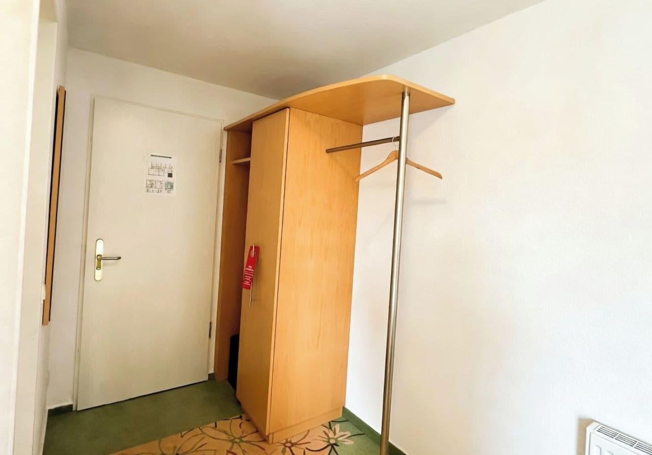 Quarto com porta, guarda-roupa de madeira e cabide de metal.