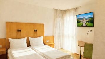 Habitación de hotel con una cama doble, una mesita de noche, una silla, un escritorio y un televisor montado en la pared.