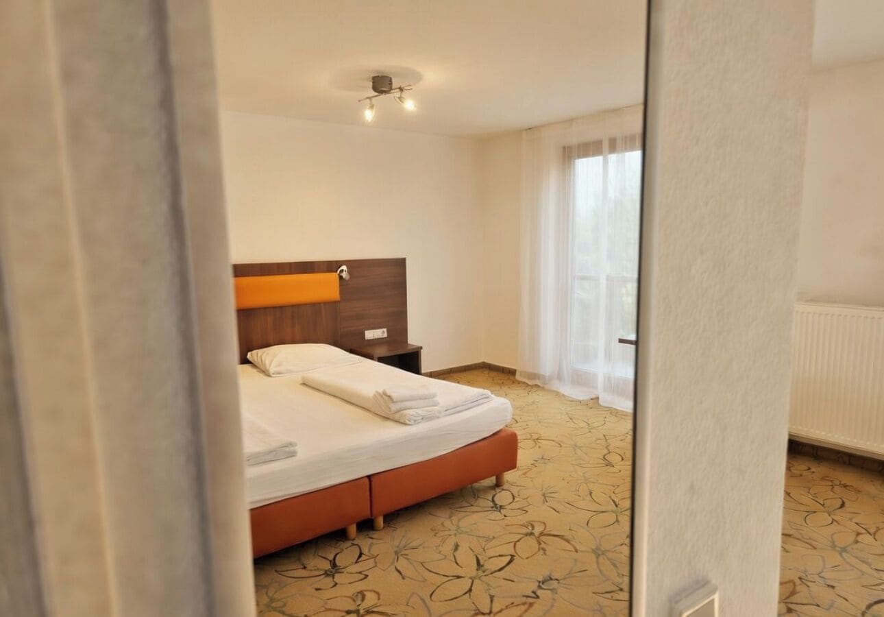A hotel room with a bed, a nightstand, a wooden headboard, and a window with curtains.