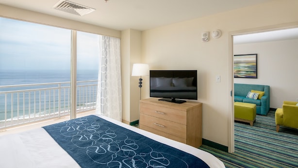 Une chambre d’hôtel avec un grand lit, une télévision, un bureau avec une lampe, une vue sur l’océan et un canapé.