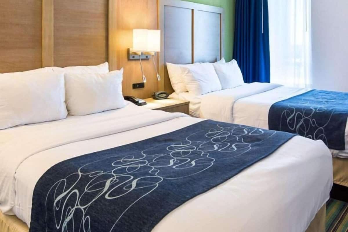 Een hotelkamer met twee bedden, een nachtkastje met een lamp en een raam met blauwe gordijnen.