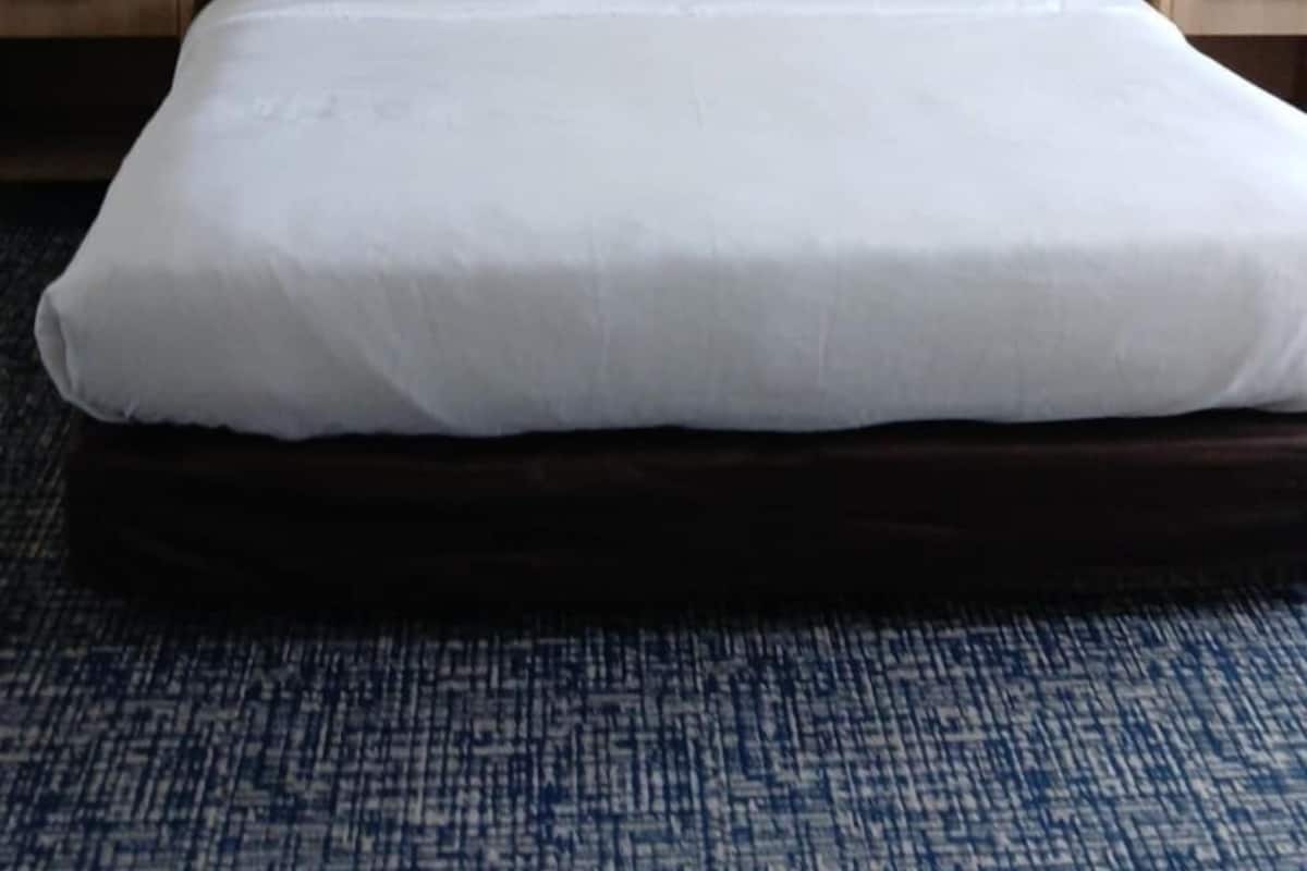 Een hotelkamer met een groot bed, een houten hoofdeinde, wit beddengoed en twee nachtkastjes met lampen.