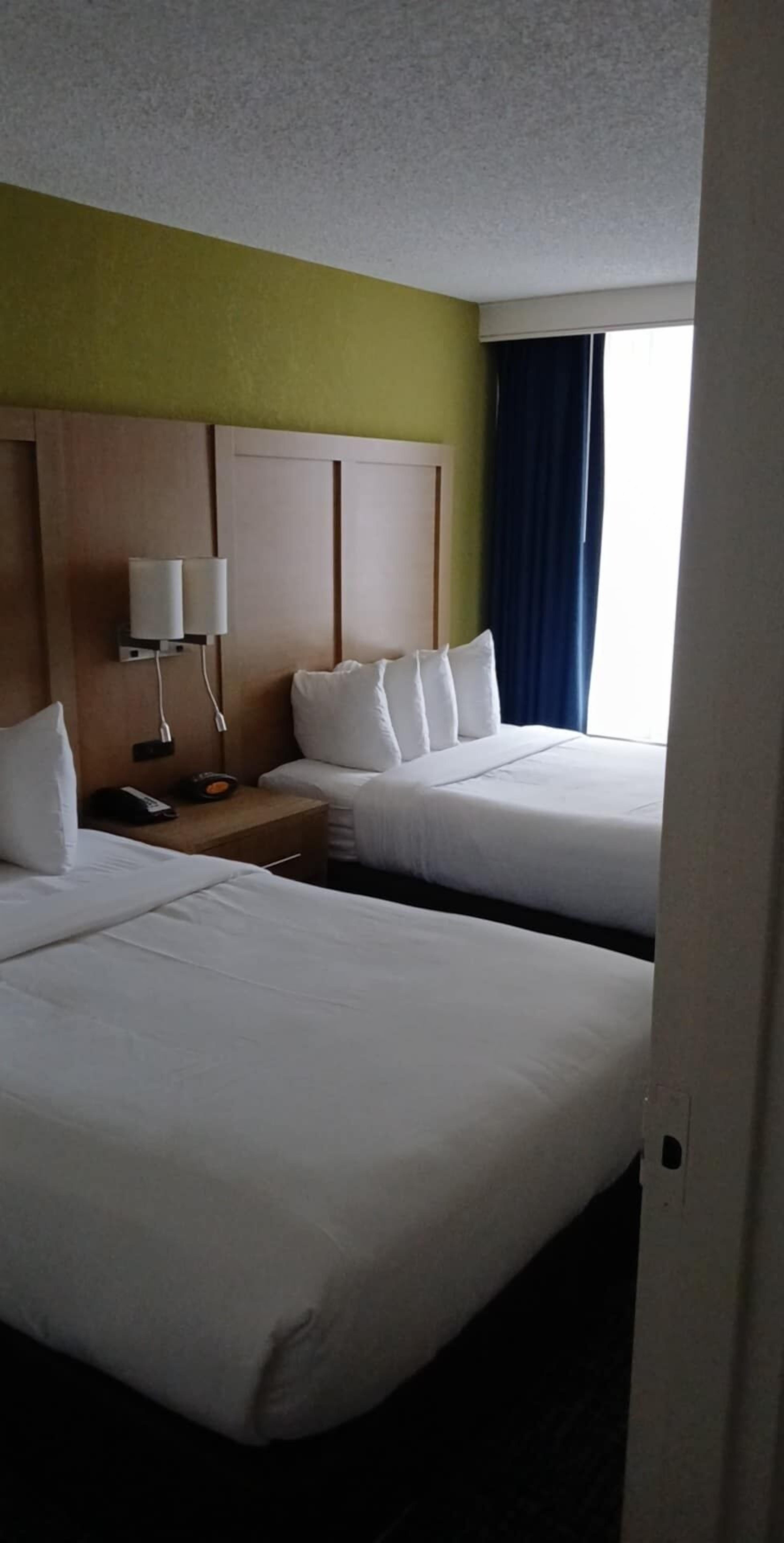 A hotel room with two beds, a nightstand with a lamp, and a window with curtains.